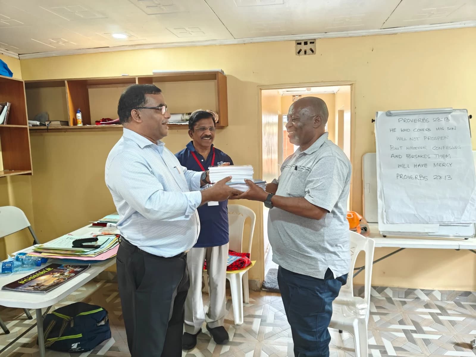 A member of the Brethren Sunday School Committee handing a stack of Sunday School books to a church leader in Africa.